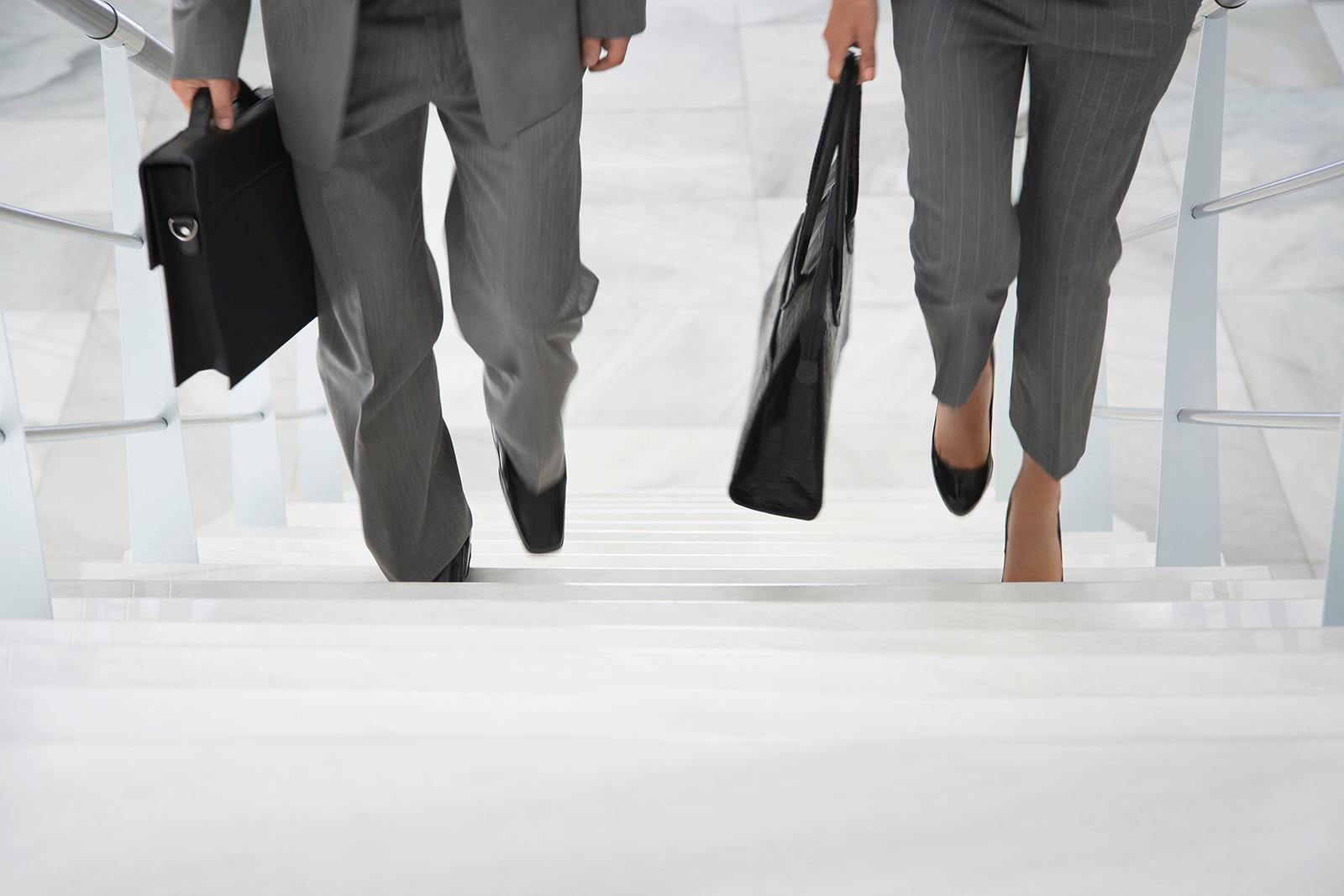 legs-only view of two businesspeople walking up stairs with briefcases in office