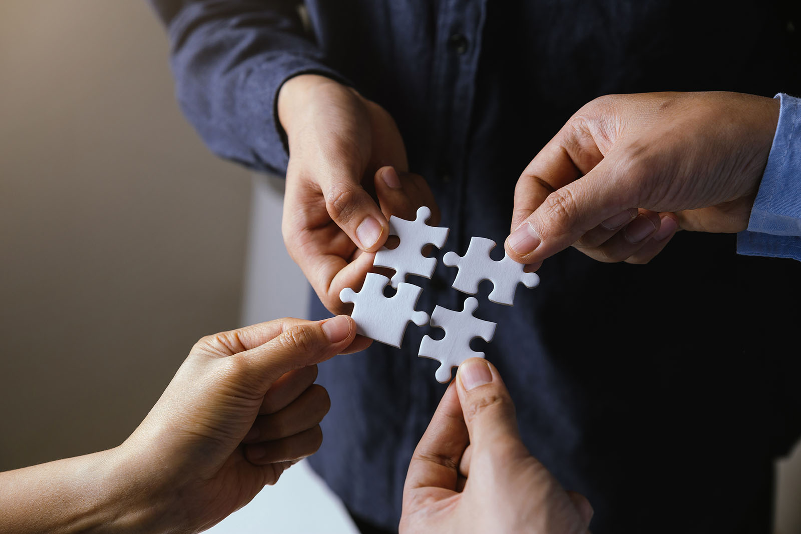 illustration of merger: four jigsaw puzzle pieces, each held by a different person's hand